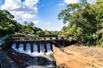 Vista aérea de uma barragem e do reservatório cercados por vegetação verde em Londrina, no Paraná.