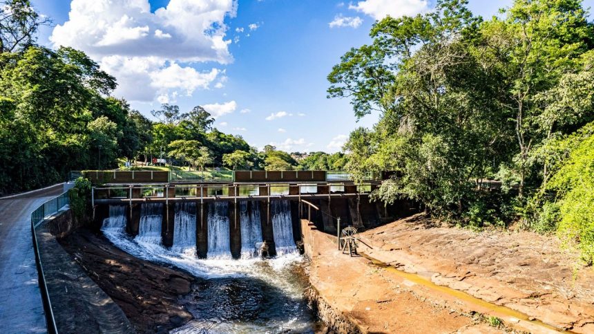 Vista aérea de uma barragem e do reservatório cercados por vegetação verde em Londrina, no Paraná.