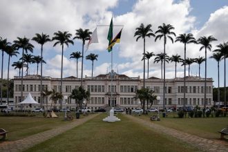 Edifício público brasileiro cercado por palmeiras sob um céu nublado.