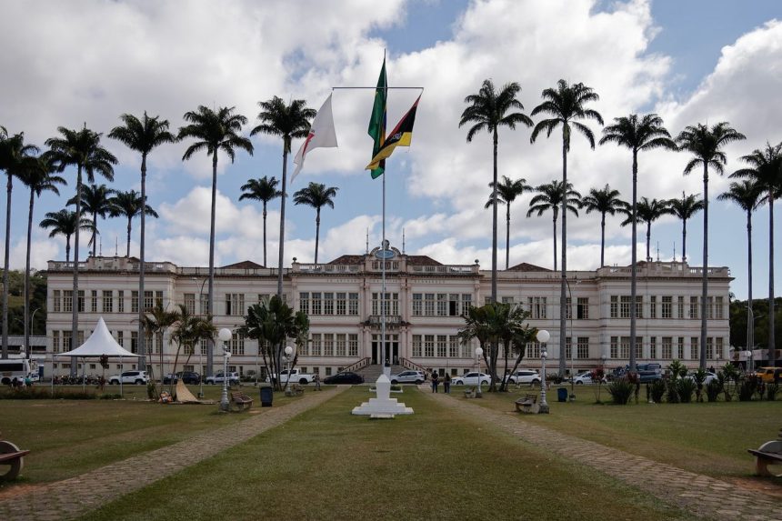 Edifício público brasileiro cercado por palmeiras sob um céu nublado.