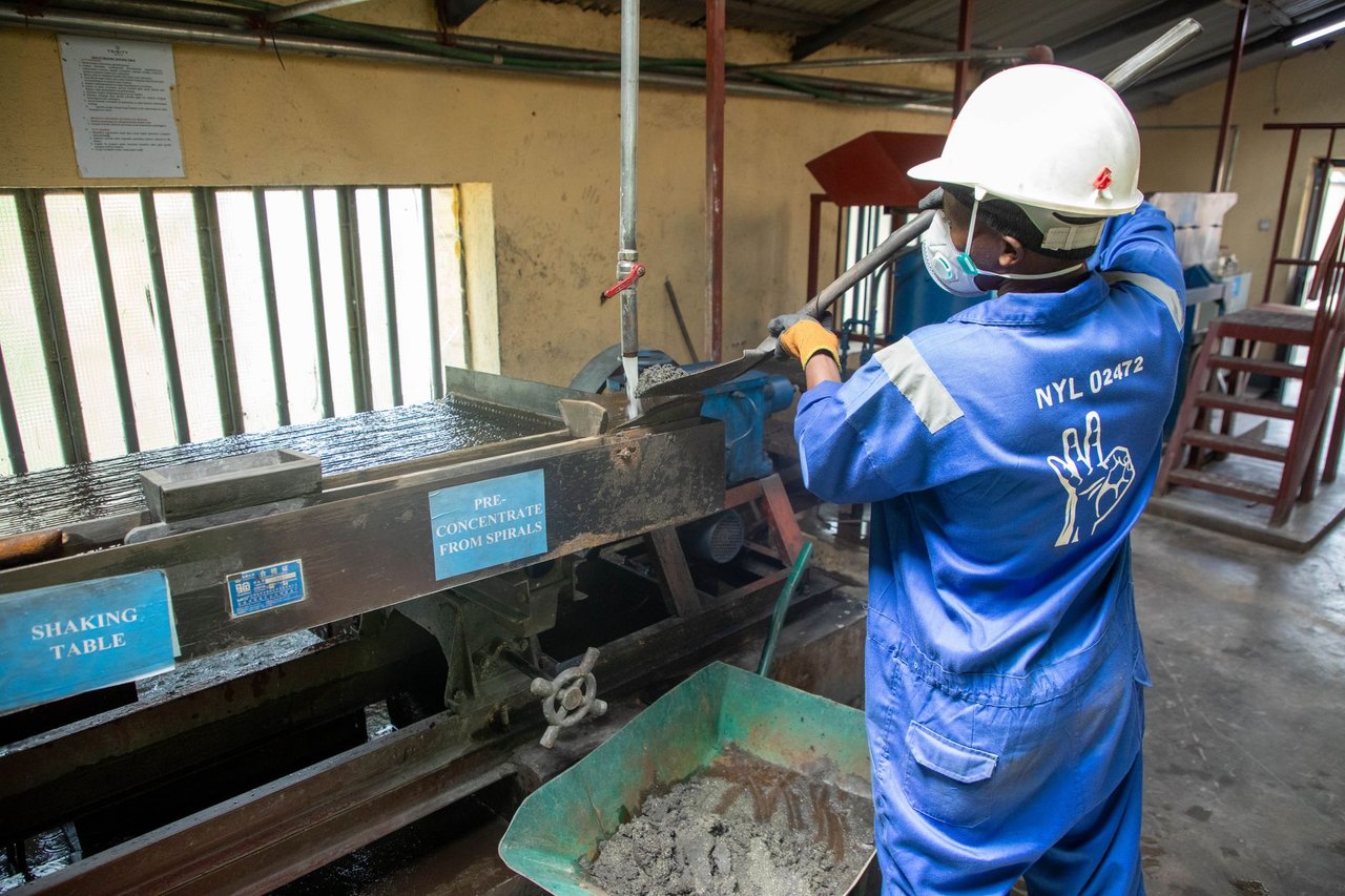 Trabalhador de macacão azul opera uma mesa vibratória para processamento de minério em uma instalação industrial.