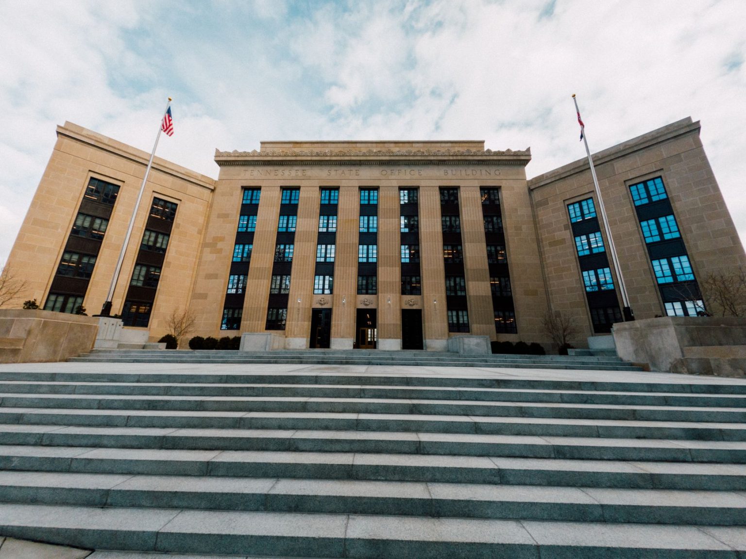 Fachada do prédio do Federal Reserve nos Estados Unidos, vista de baixo, com bandeiras americanas e céu nublado