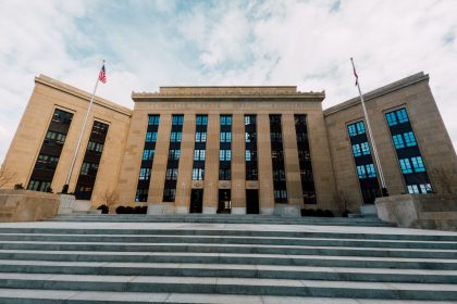 Fachada do prédio do Federal Reserve nos Estados Unidos, vista de baixo, com bandeiras americanas e céu nublado